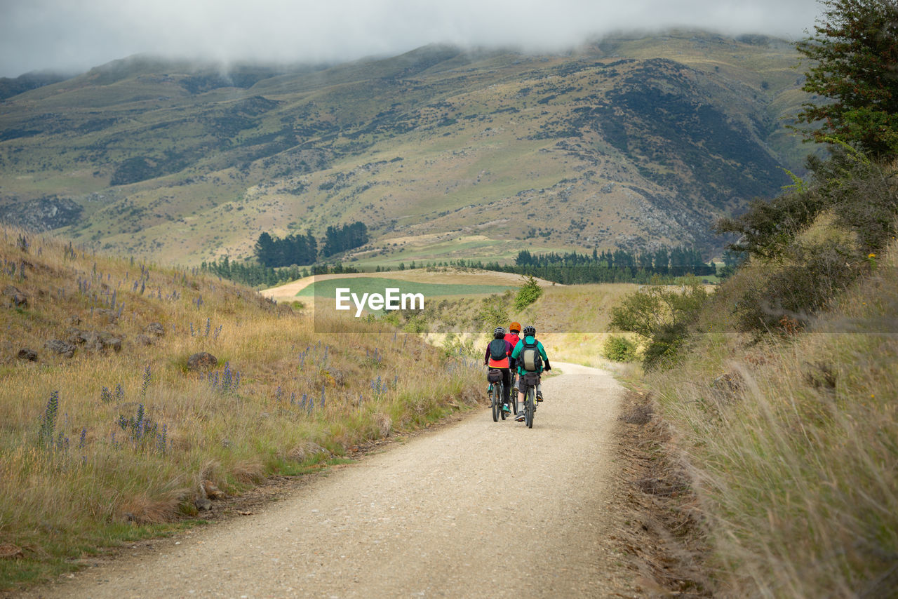 REAR VIEW OF MEN RIDING BICYCLE ON MOUNTAIN ROAD