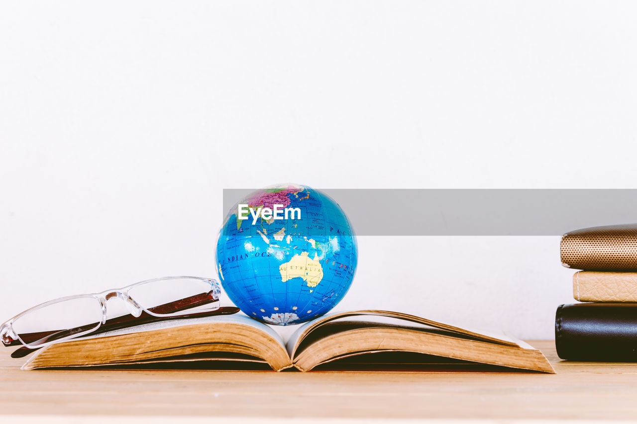 Close-up of book with globe and eyeglasses on table against white background