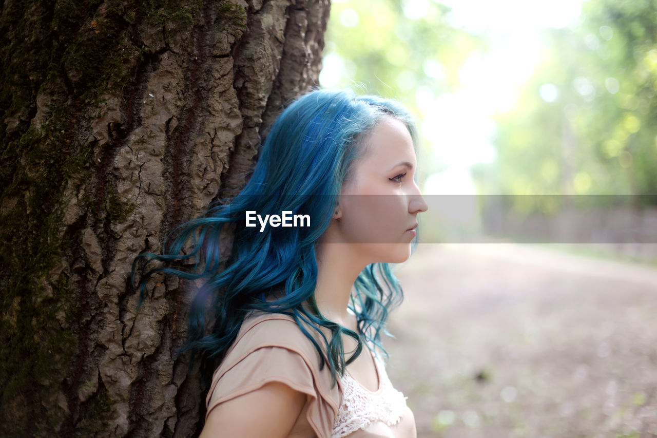 Close-up of beautiful young woman against tree trunk