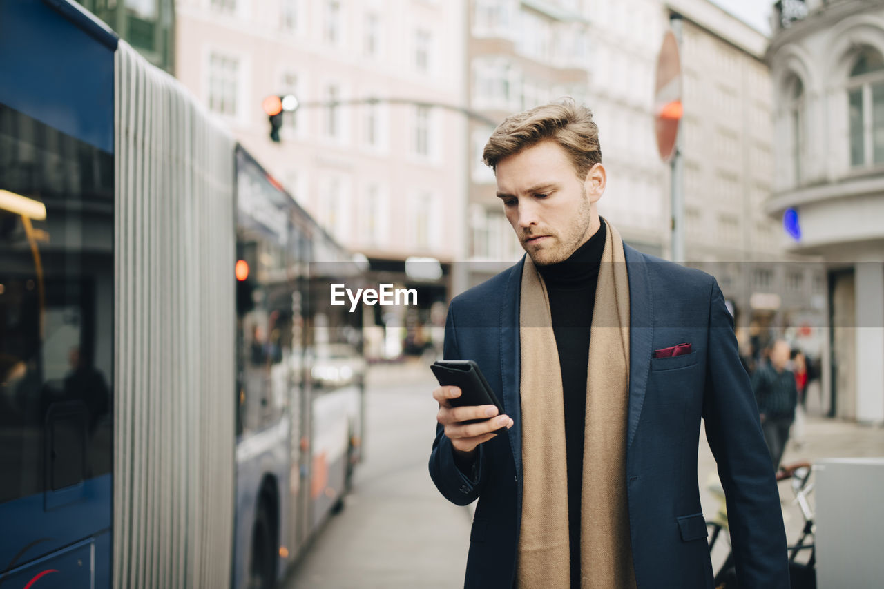 Male entrepreneur using internet through mobile phone while standing by bus in city