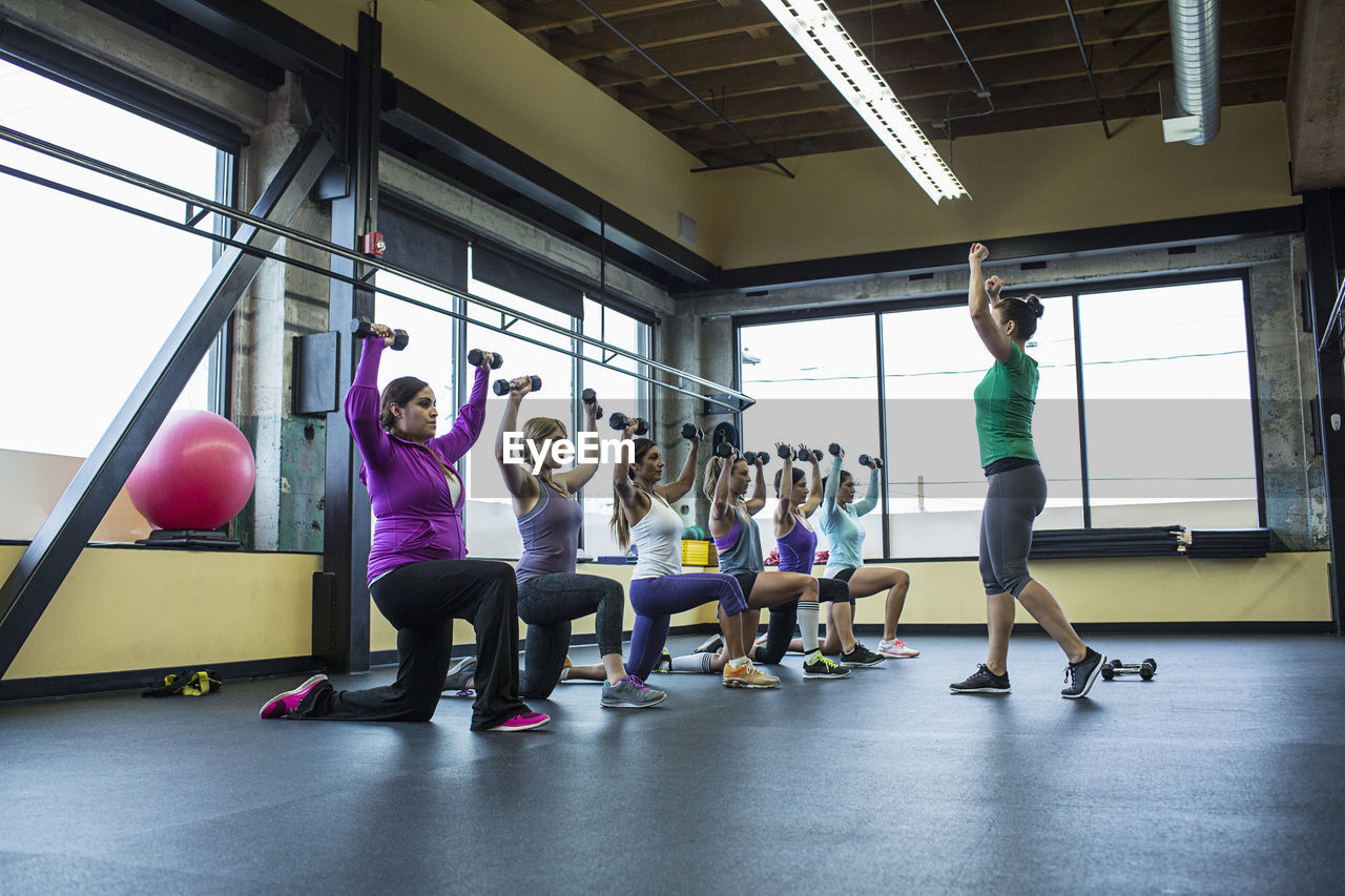 Fitness instructor guiding women in lifting dumbbells at gym