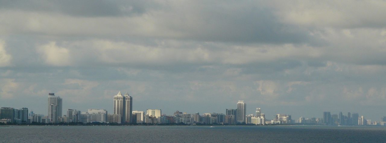 Sea and buildings against cloudy sky in city