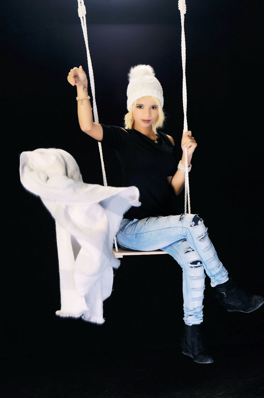 Portrait of woman throwing scarf while sitting on swing against black background