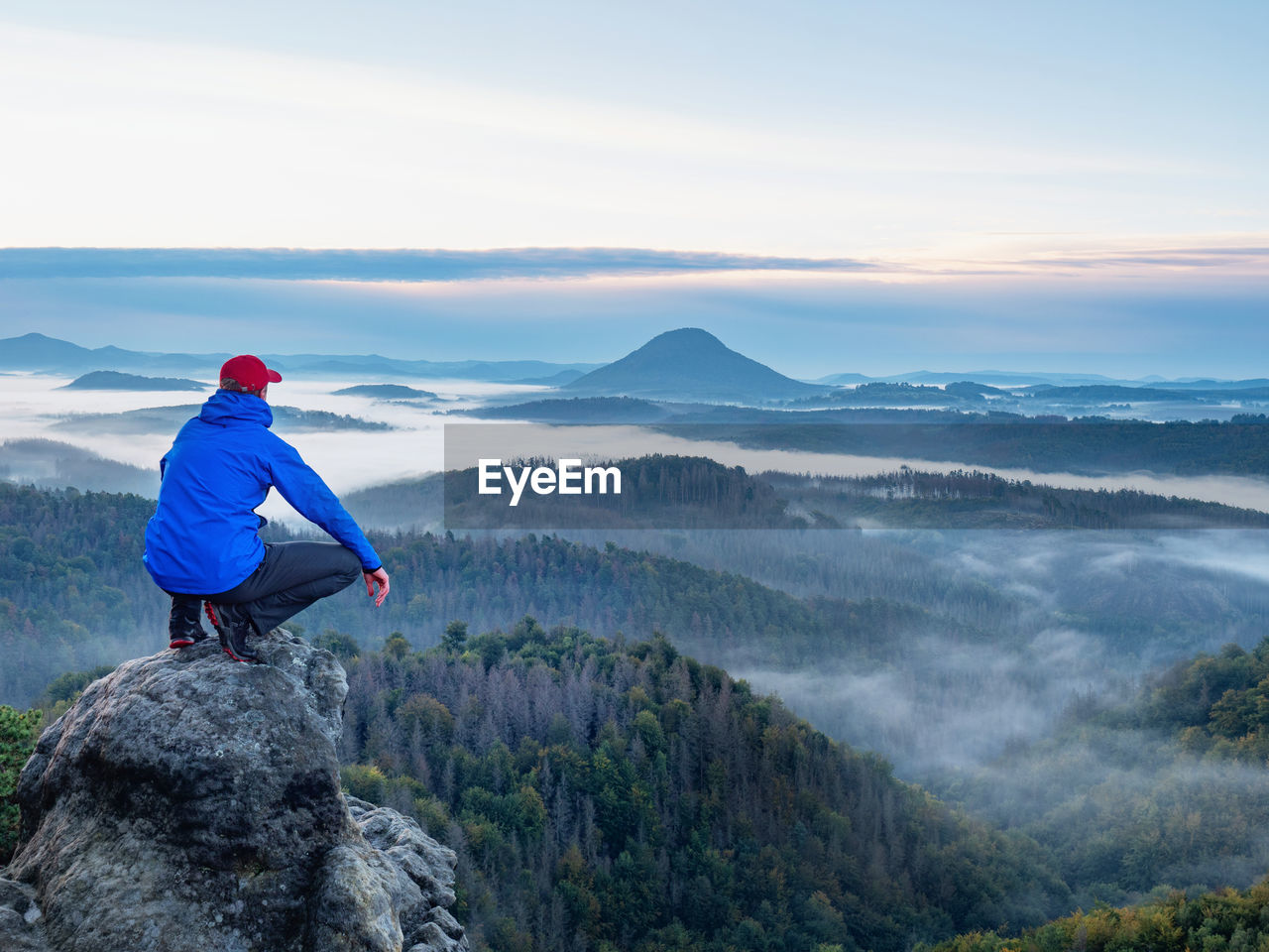 Sitting man on sharp rocky edge, enjoy amazing birds view. misty fall landscape bellow.