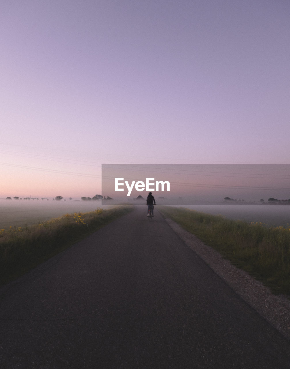 Rear view of man biking on road against sky