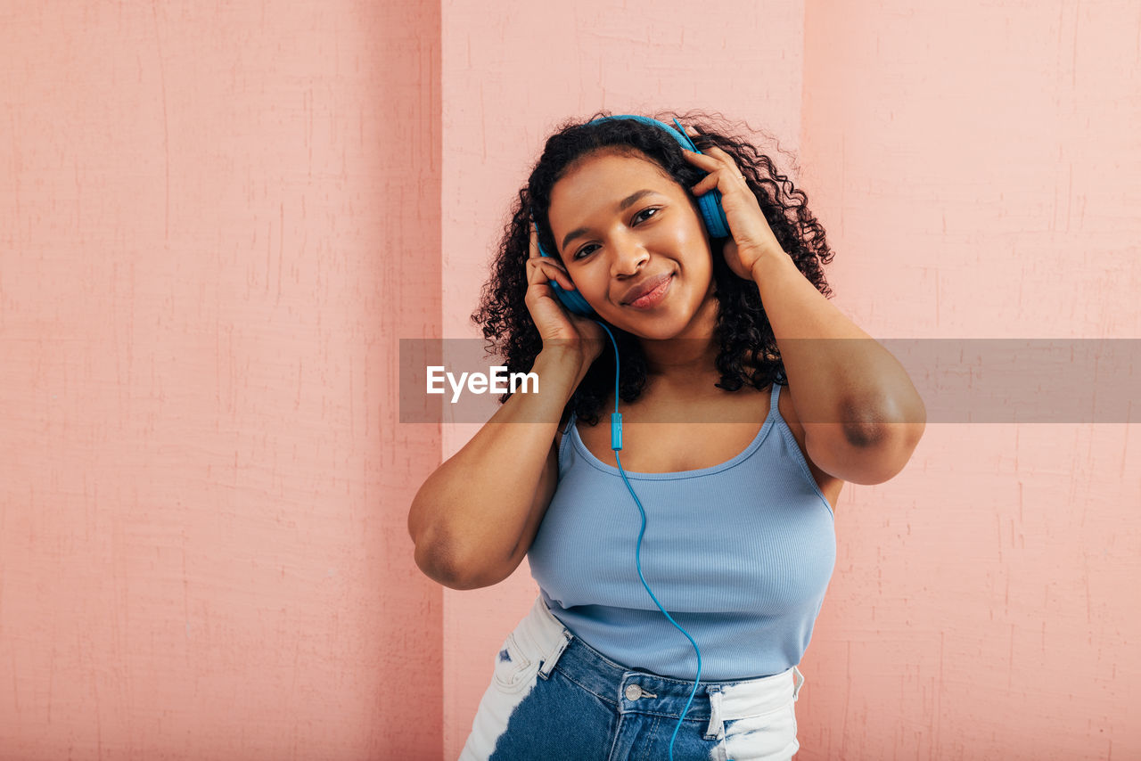 Portrait of young woman listening music standing against wall