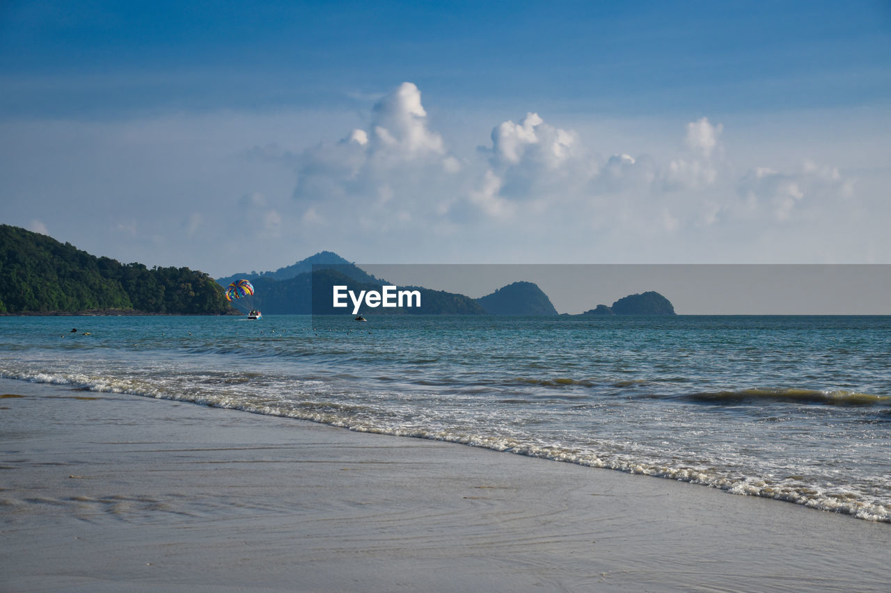 Waves of the azure andaman sea under the blue sky reaching the shores of cenang beach