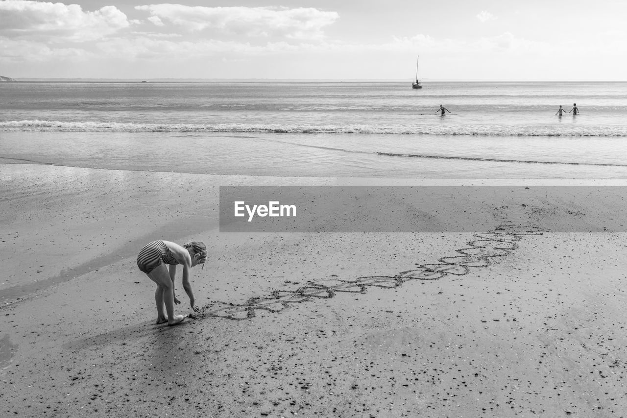 Girl making design on wet sand at beach against sky