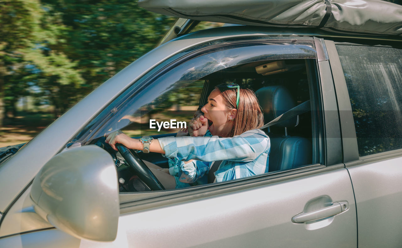 Young woman yawning while traveling in car