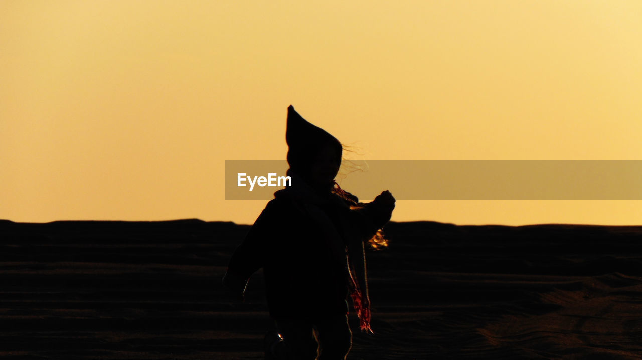 Rear view of silhouette woman standing on land against sky during sunset