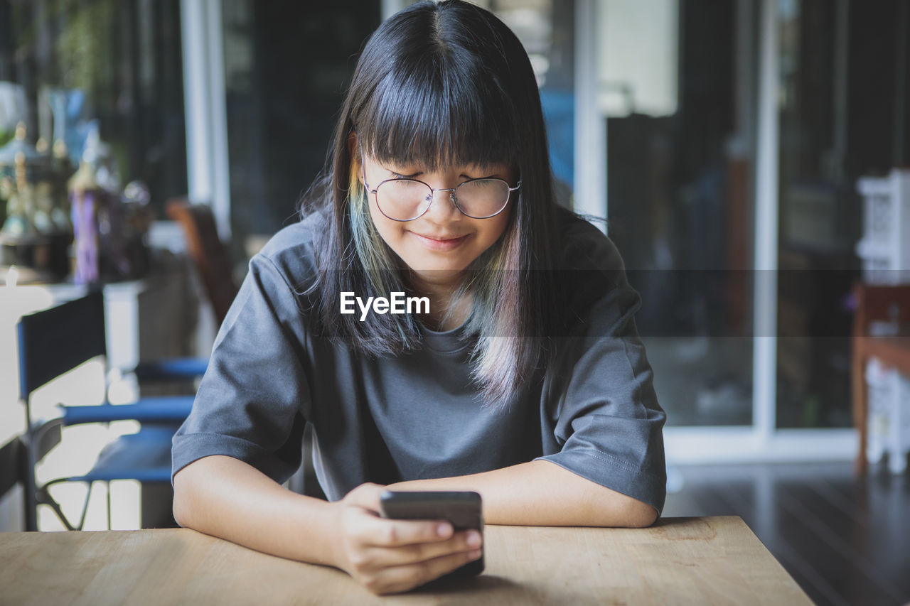 Smiling girl using mobile phone while sitting at cafe