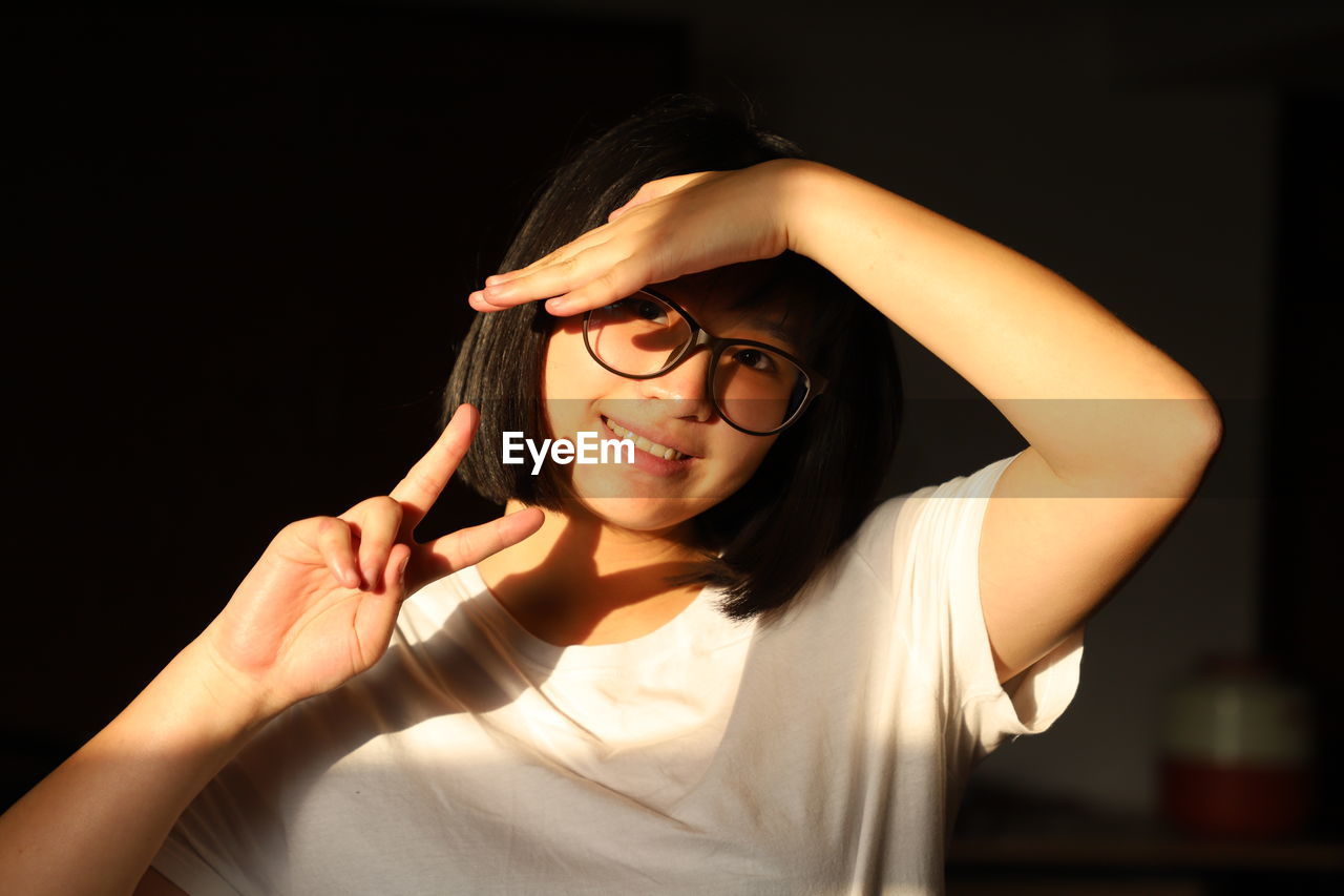 Close-up portrait of young woman shielding eyes while gesturing at home