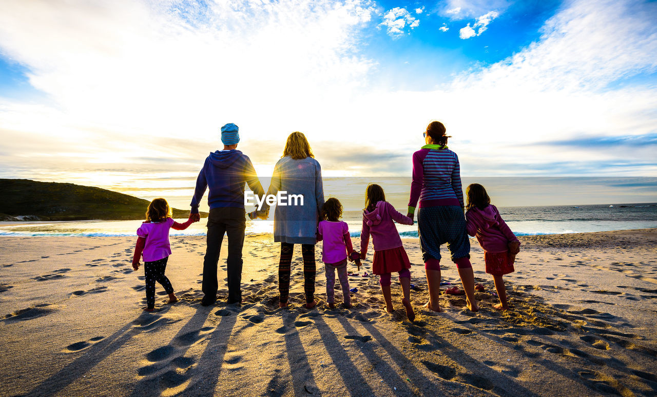 Rear view of people holding hands while standing at beach against sky