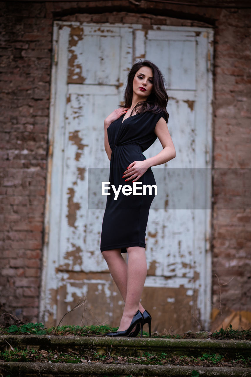 Full length portrait of woman standing against brick wall