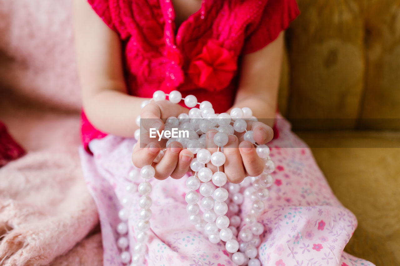 Midsection of woman with beads sitting on bed