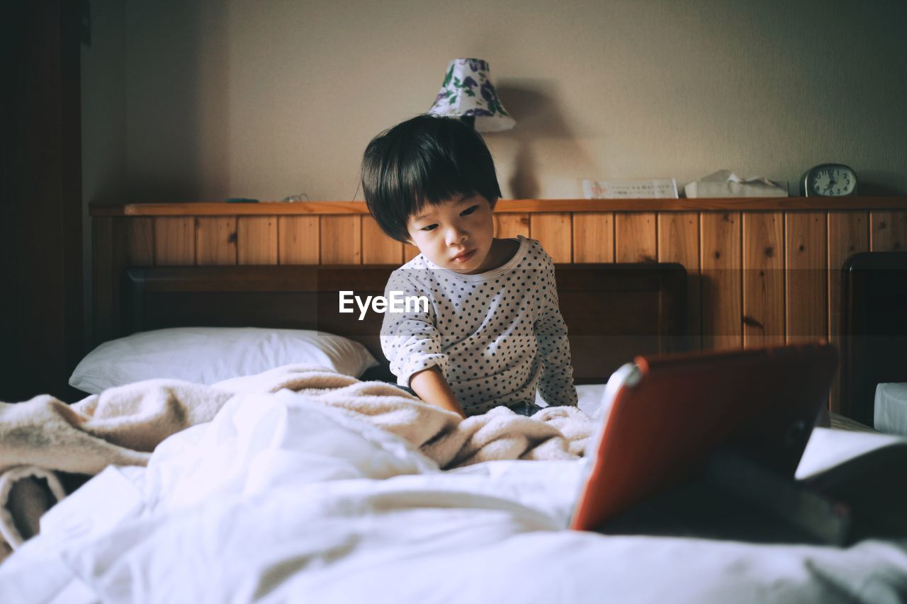 Boy watching video over digital tablet while sitting on bed at home