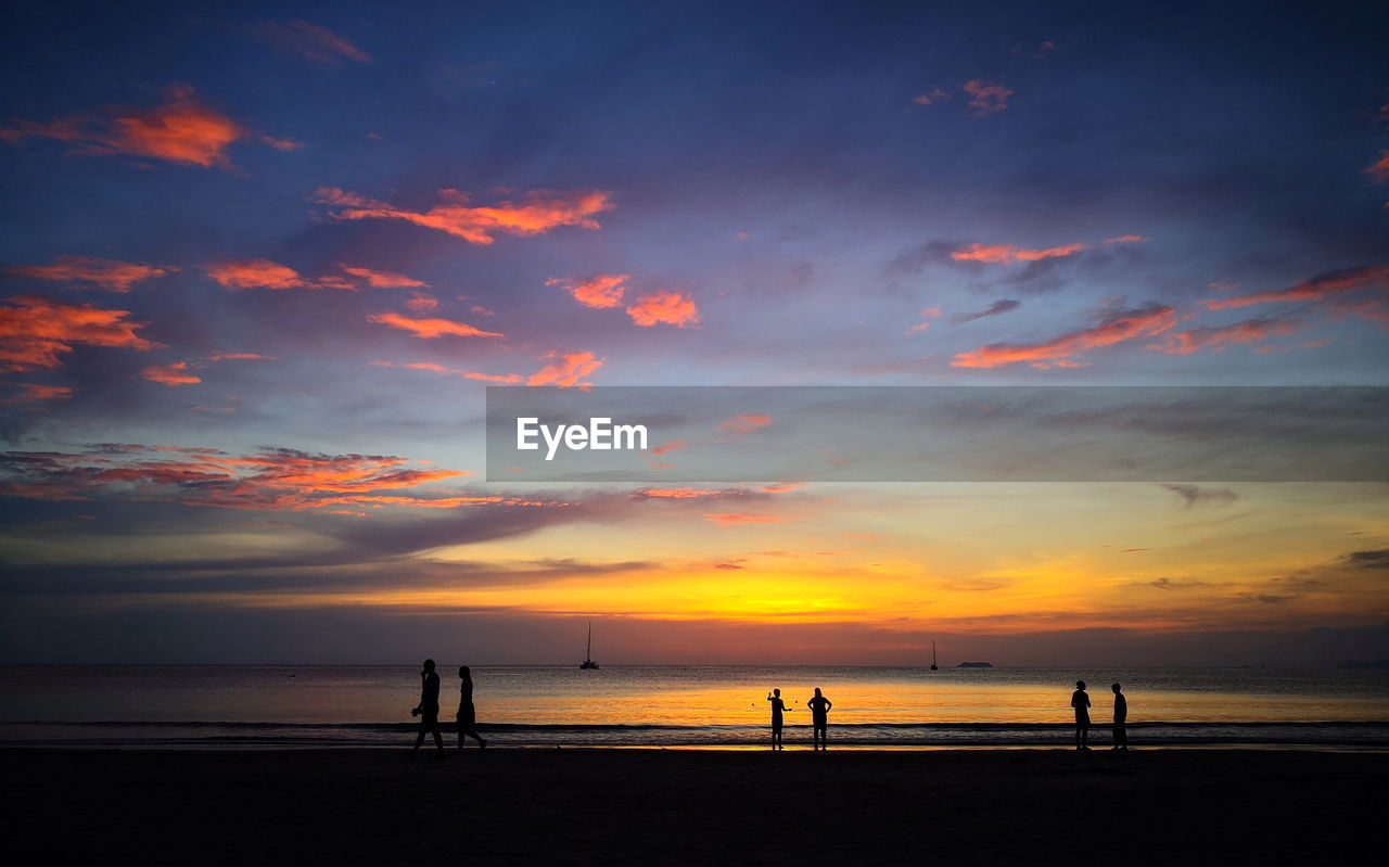 SILHOUETTE PEOPLE ON BEACH AGAINST ORANGE SKY