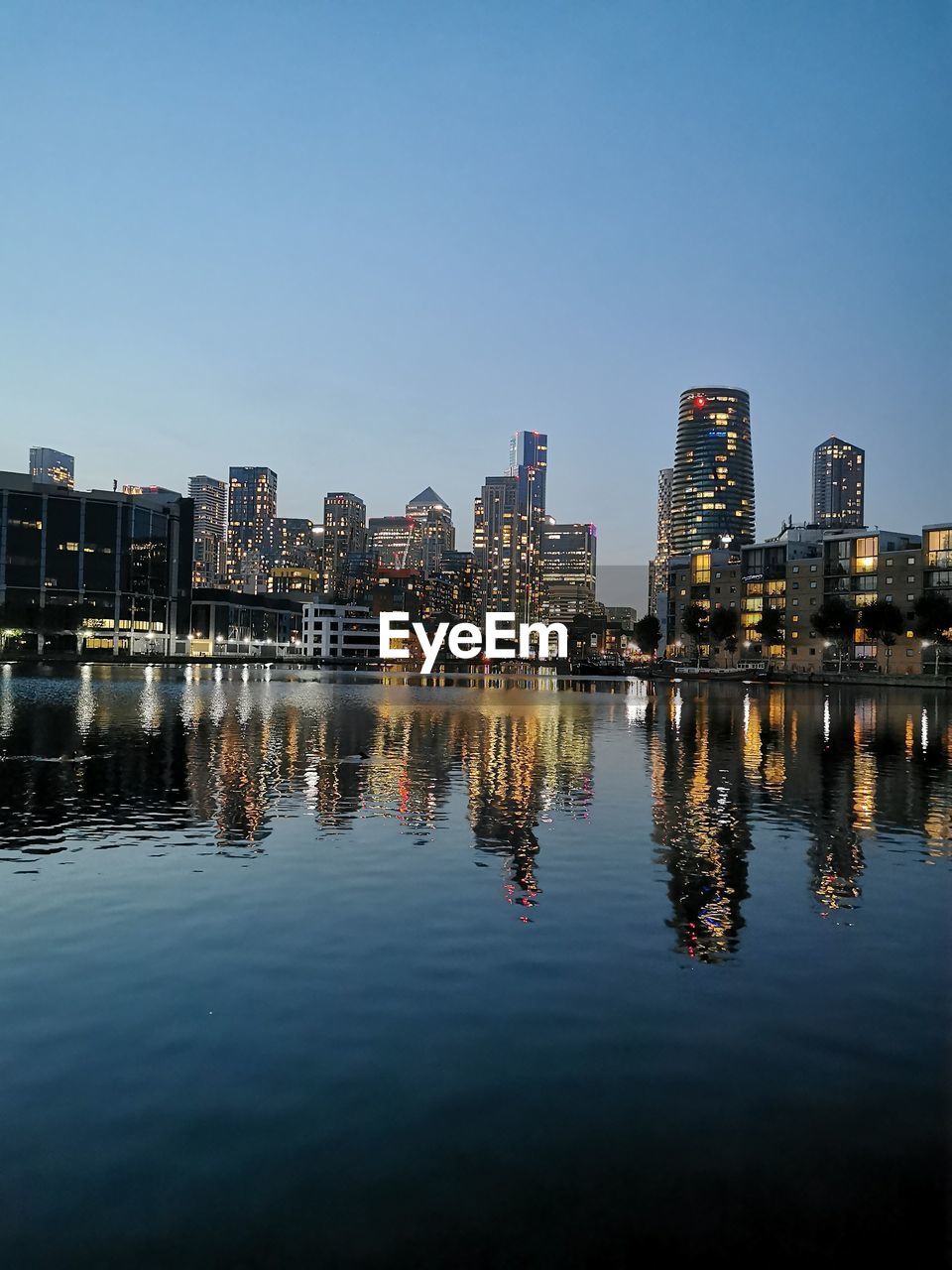 ILLUMINATED BUILDINGS BY RIVER AGAINST SKY IN CITY