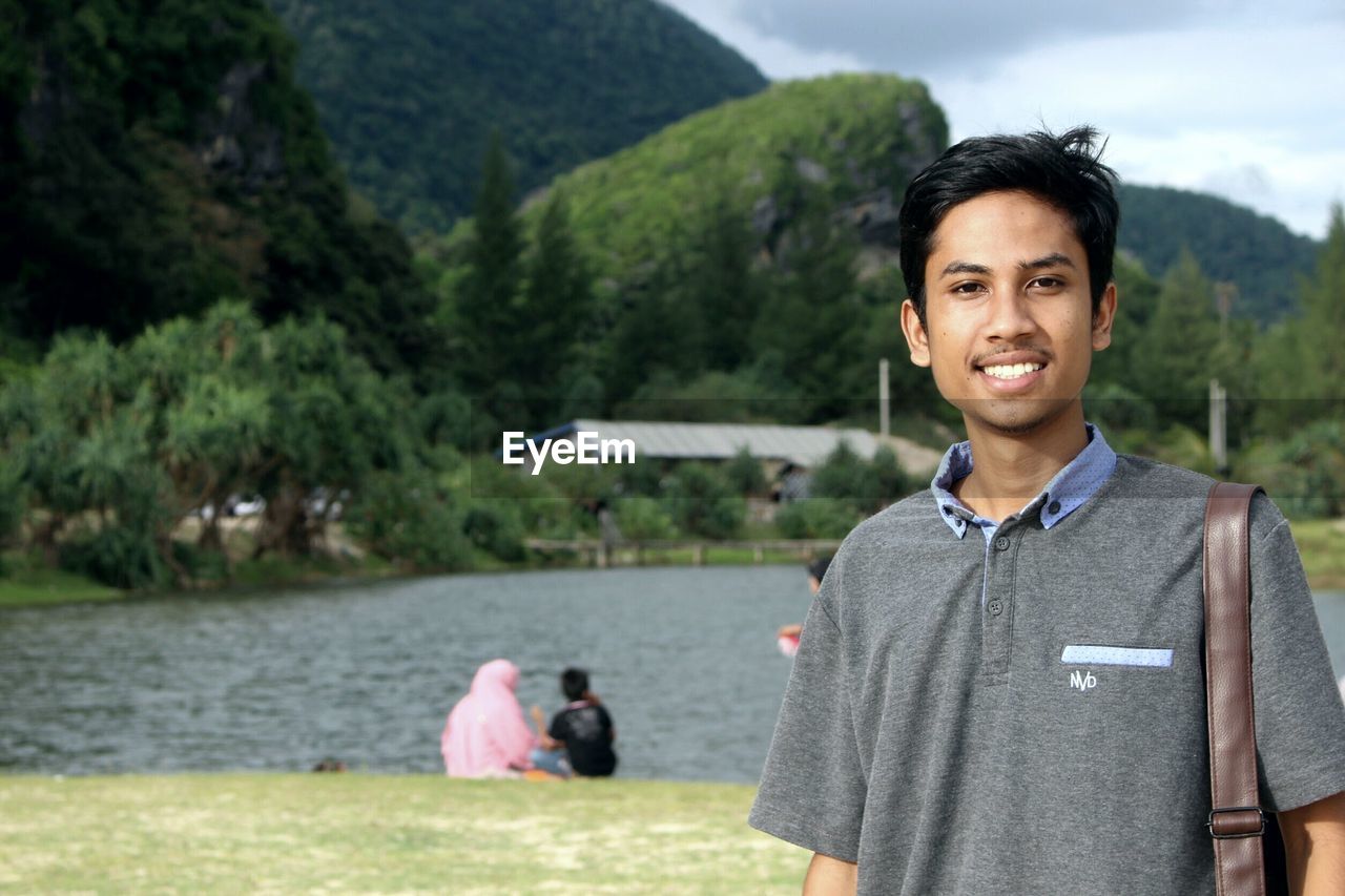 PORTRAIT OF A SMILING YOUNG MAN AGAINST TREES