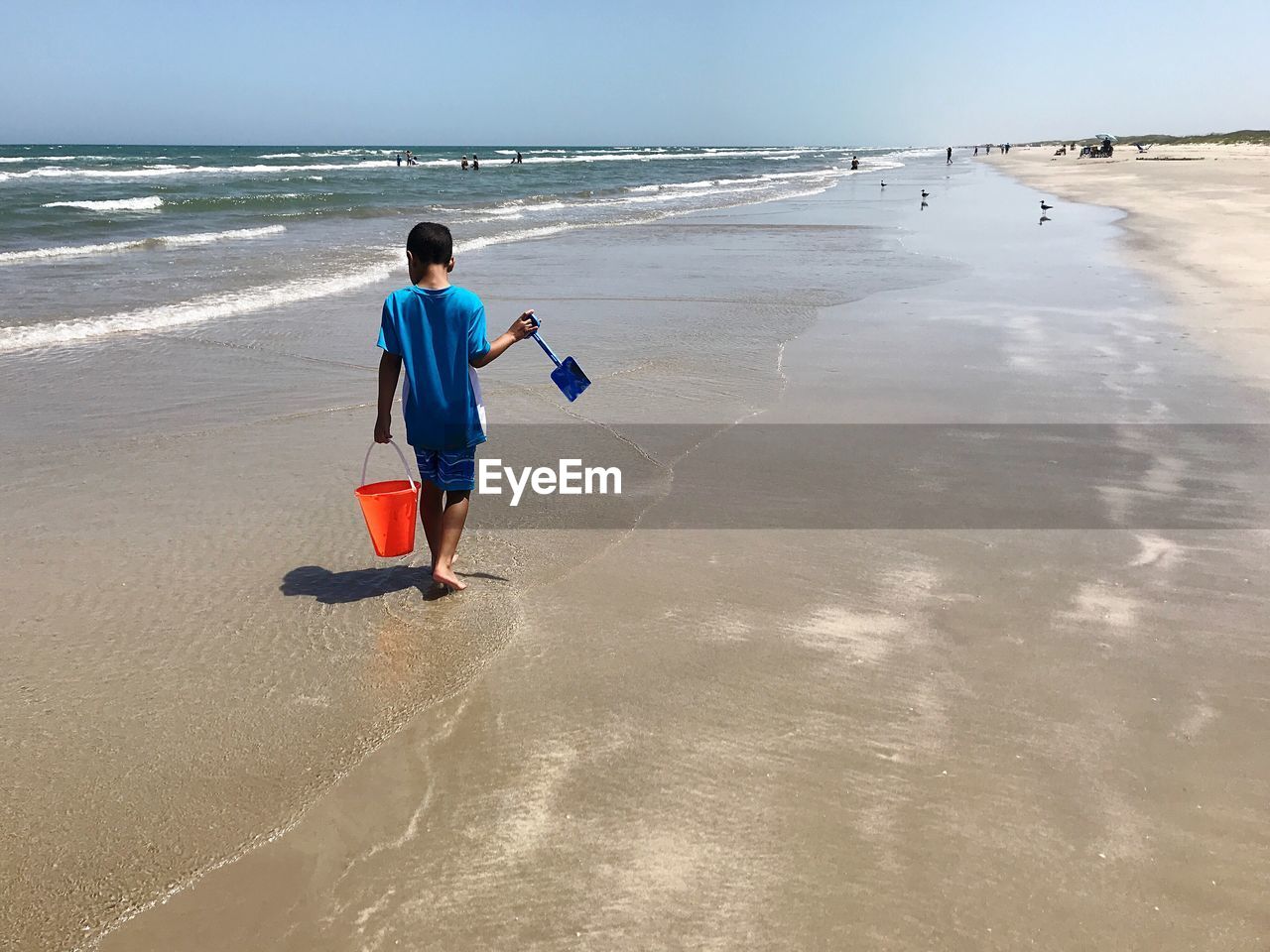 Rear view of boy with bucket walking on beach against sky