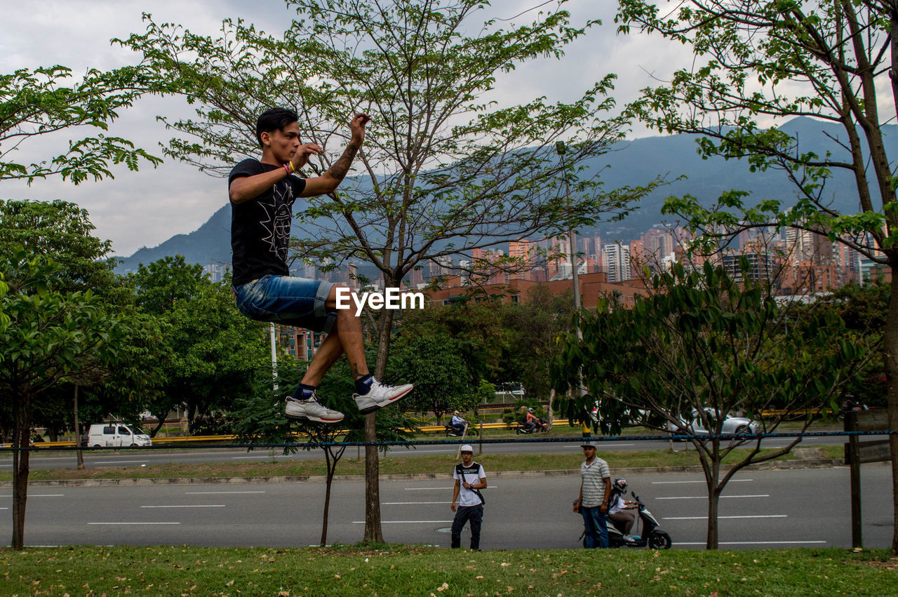 FULL LENGTH OF YOUNG MAN JUMPING ON TREE