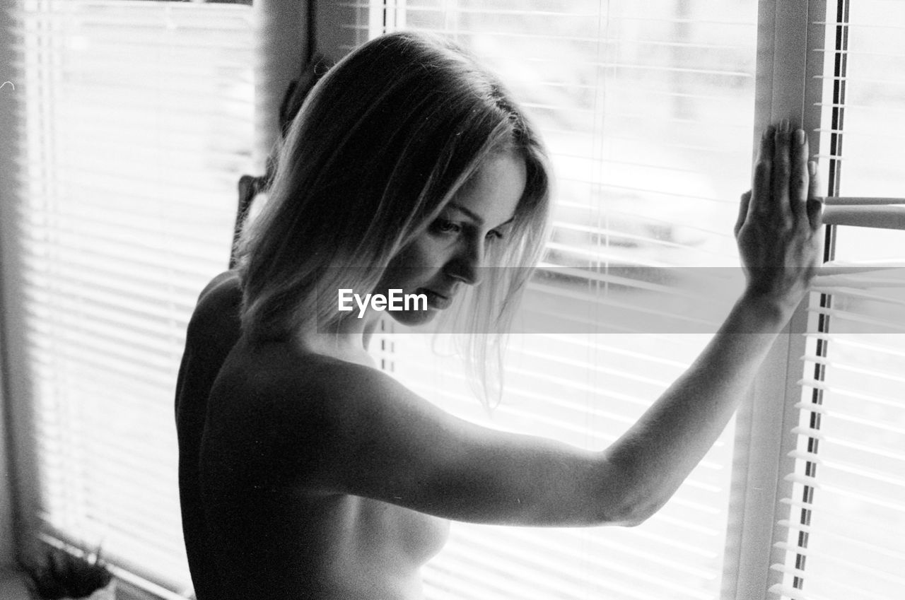 Side view of thoughtful naked woman standing by window