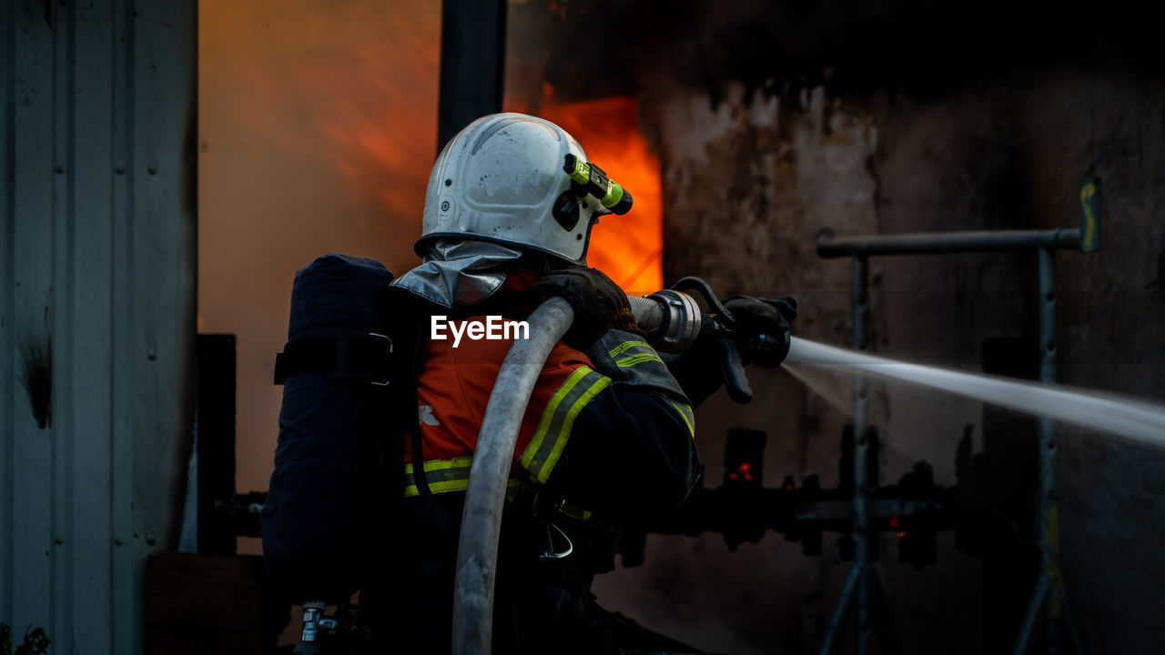 Rear view of fireman splashing water from fire hose