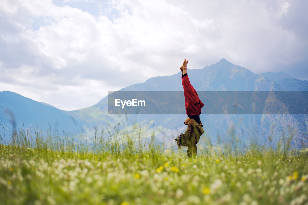 Side view of woman doing handstand on grassy field against mountains