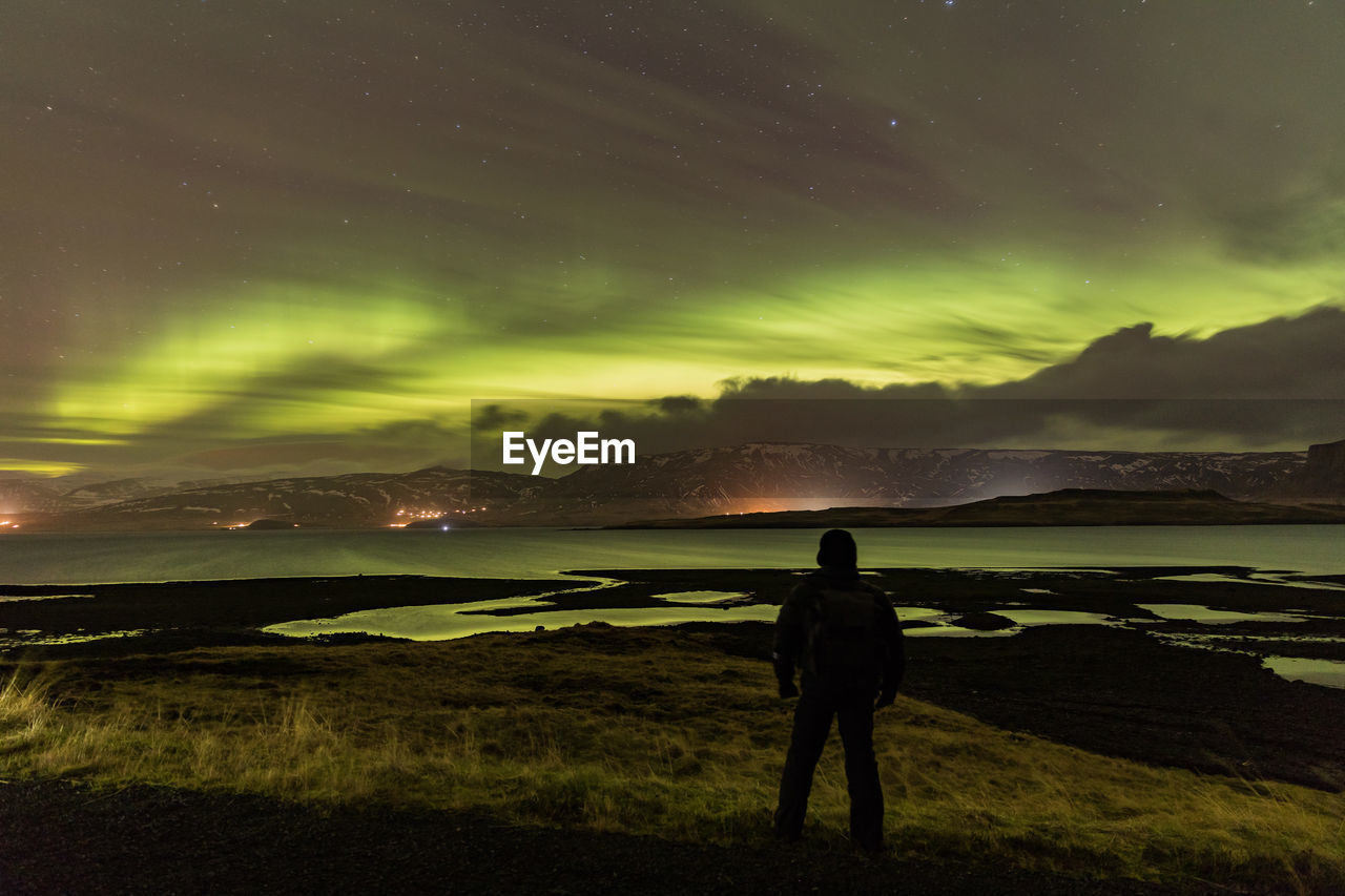 Rear view of man standing on landscape against sky at night