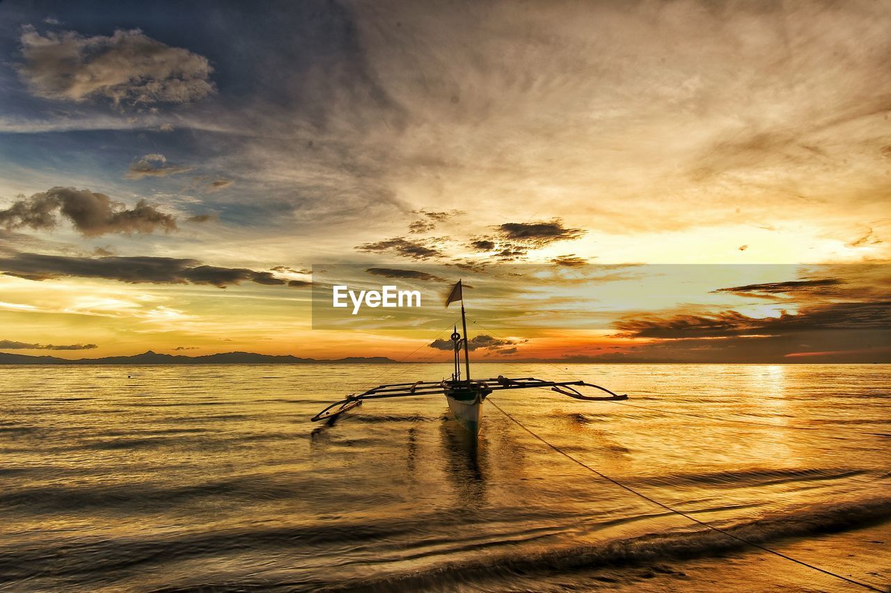 Boat on sea against cloudy sky during sunset