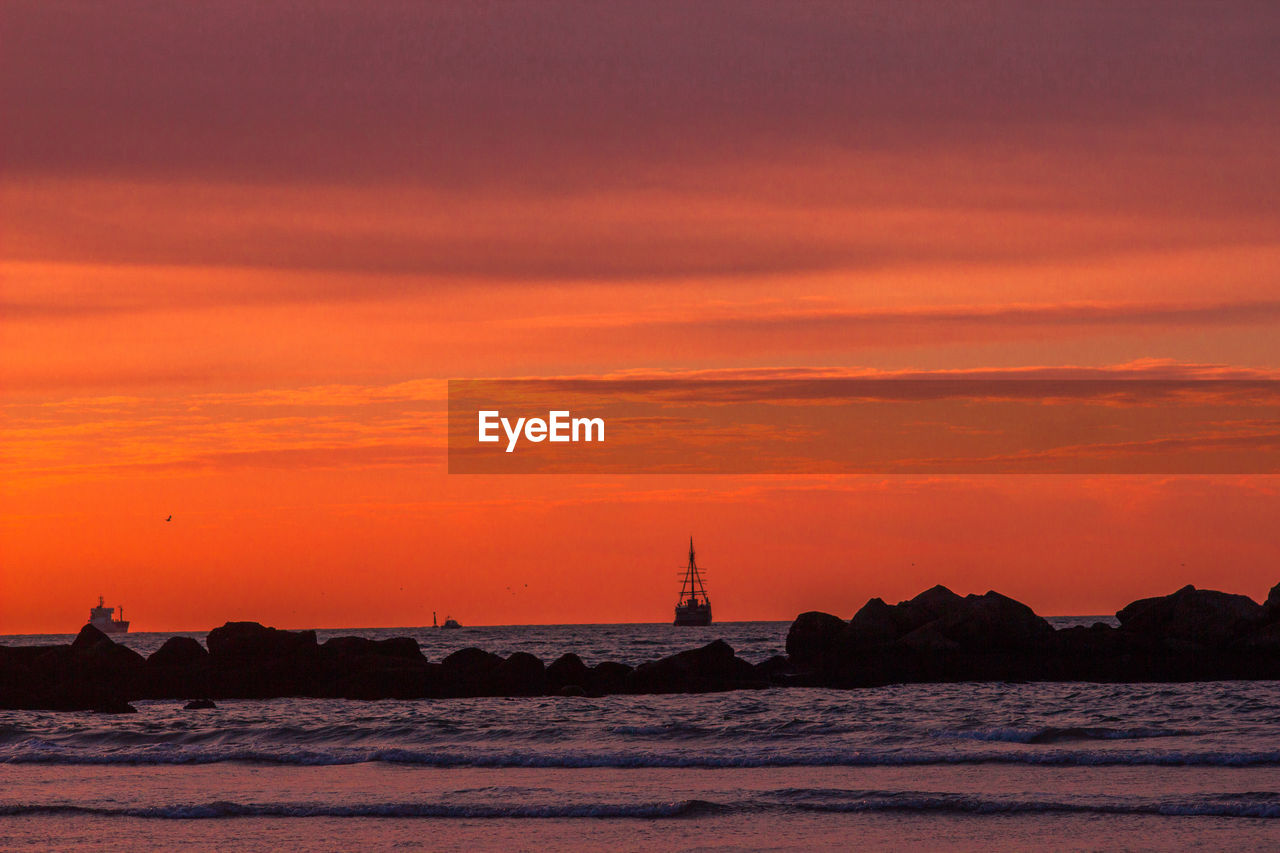 Silhouette sailboats on sea against orange sky