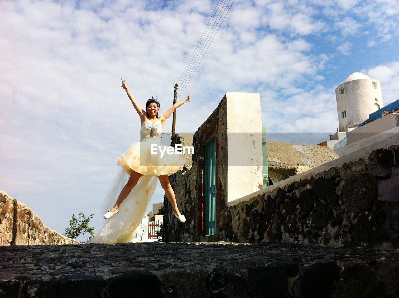 Full length of happy bride jumping on street against sky