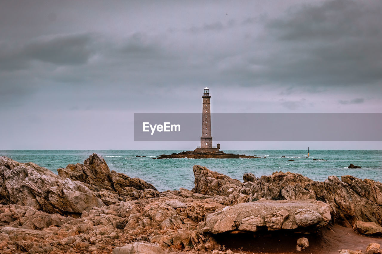 Lighthouse on rock by sea against sky