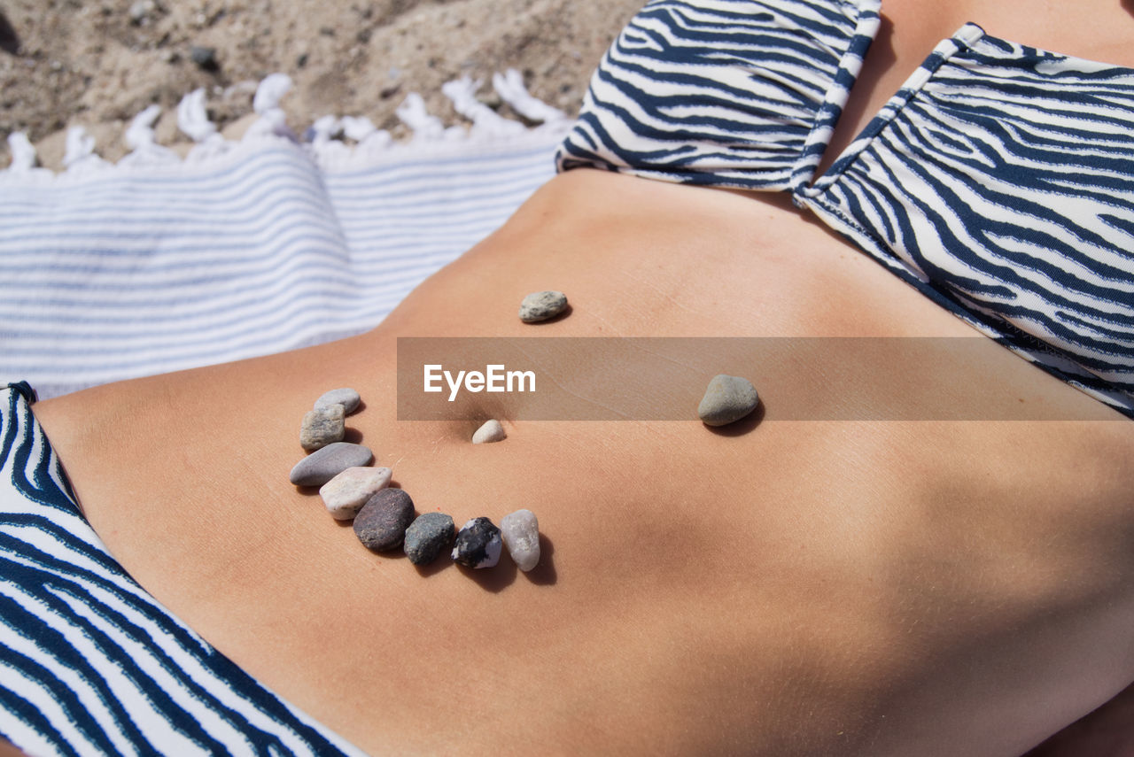 Midsection of woman with pebbles on stomach at beach