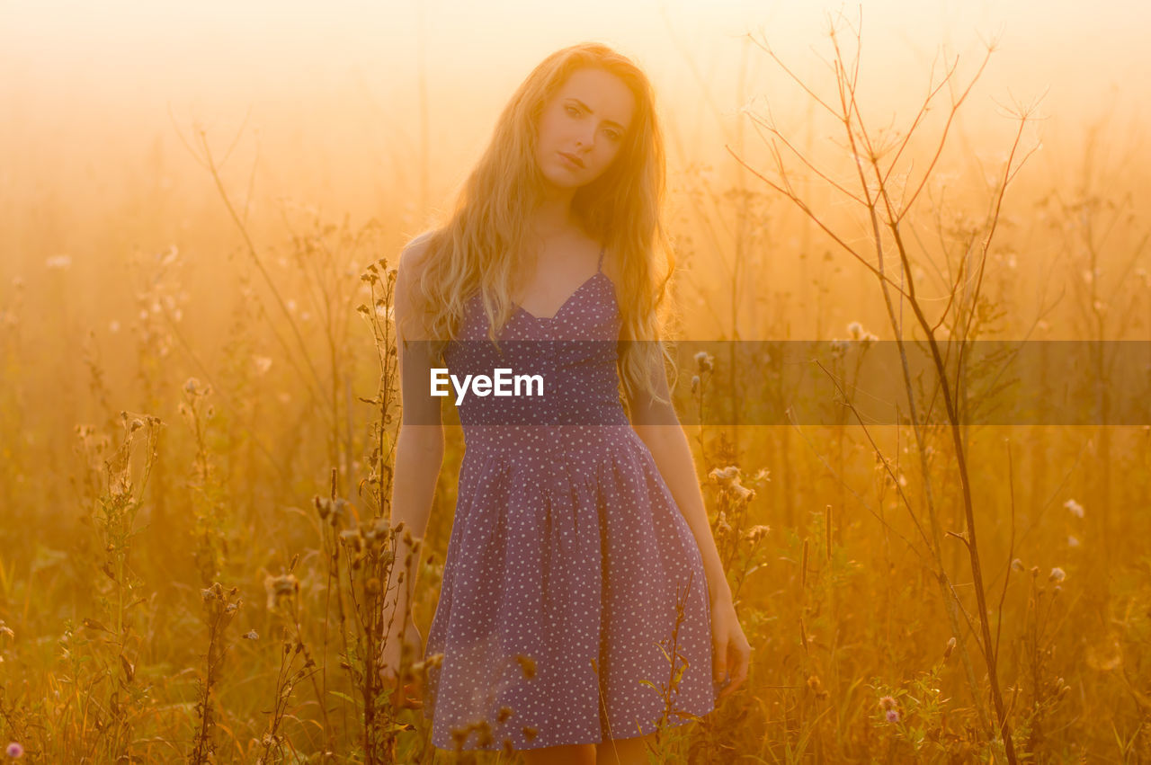 PORTRAIT OF WOMAN STANDING ON FIELD IN SUNLIGHT