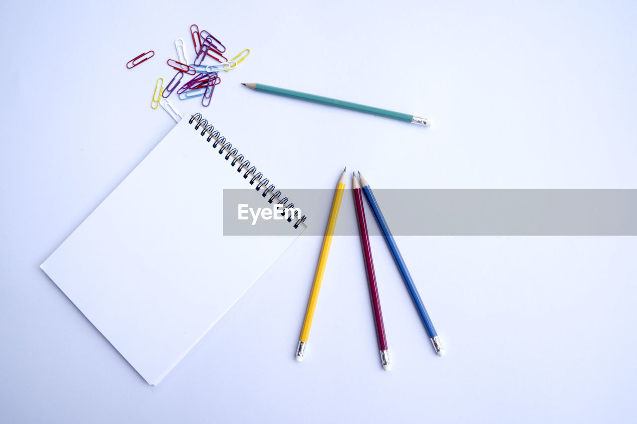 Directly above shot of colorful pencils and note pad on white background