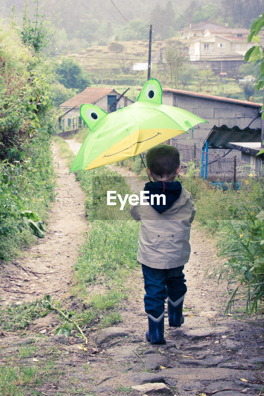 Rear view of boy holding umbrella while walking on footpath