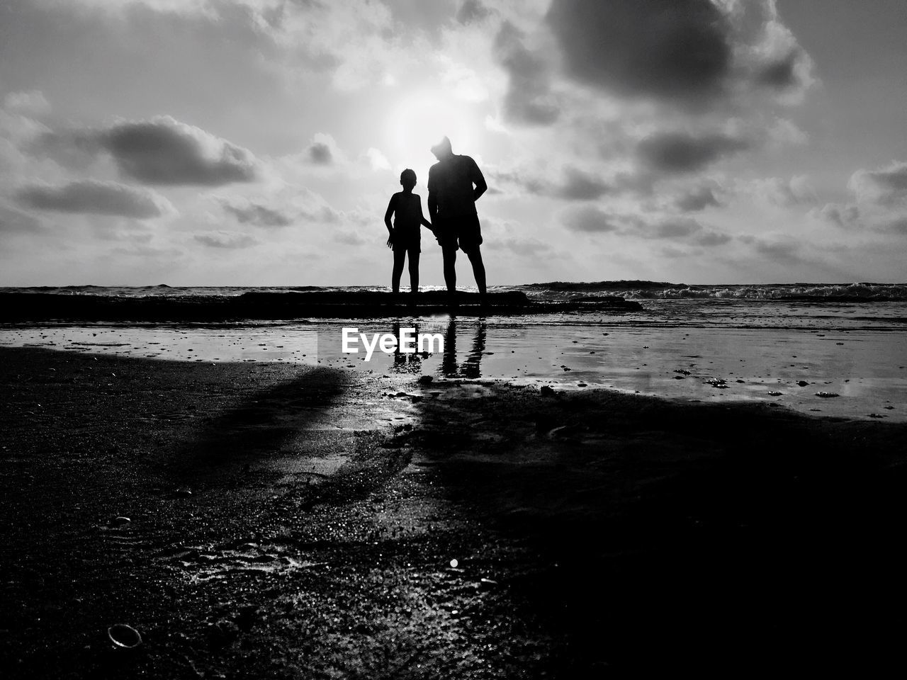 Man with son standing at beach against sky