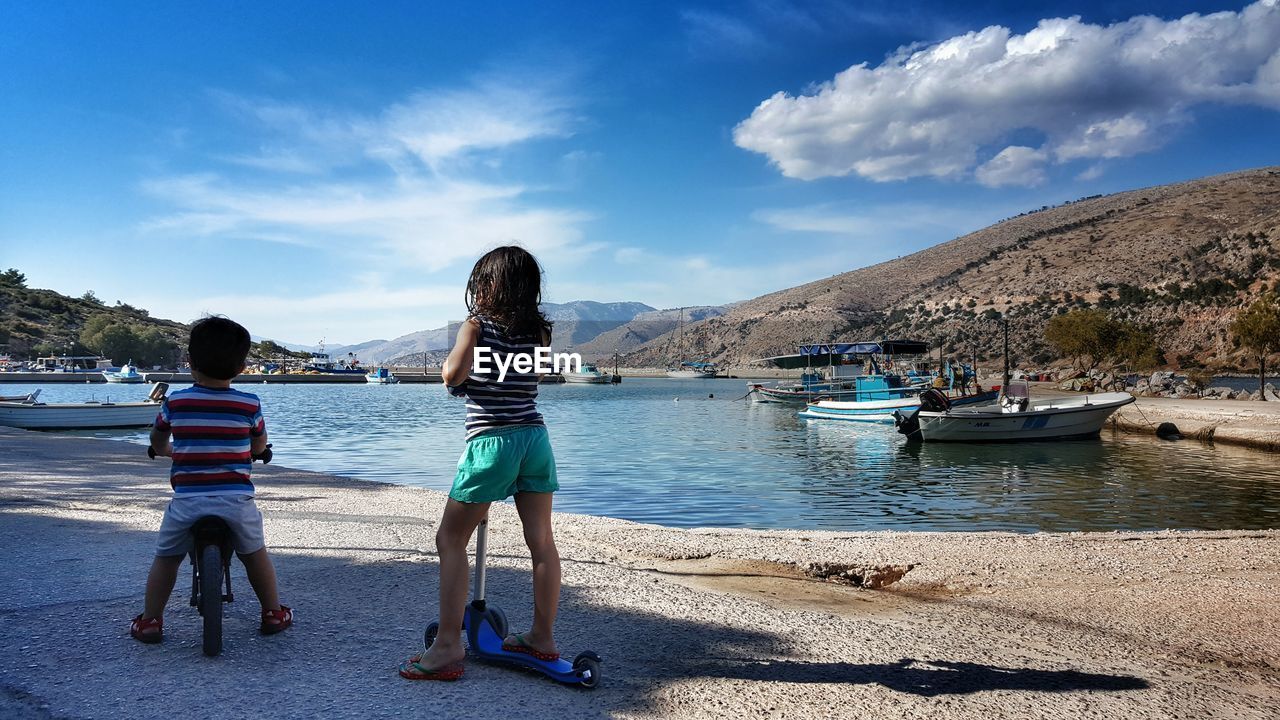 Rear view of girl with push scooter by boy against lake