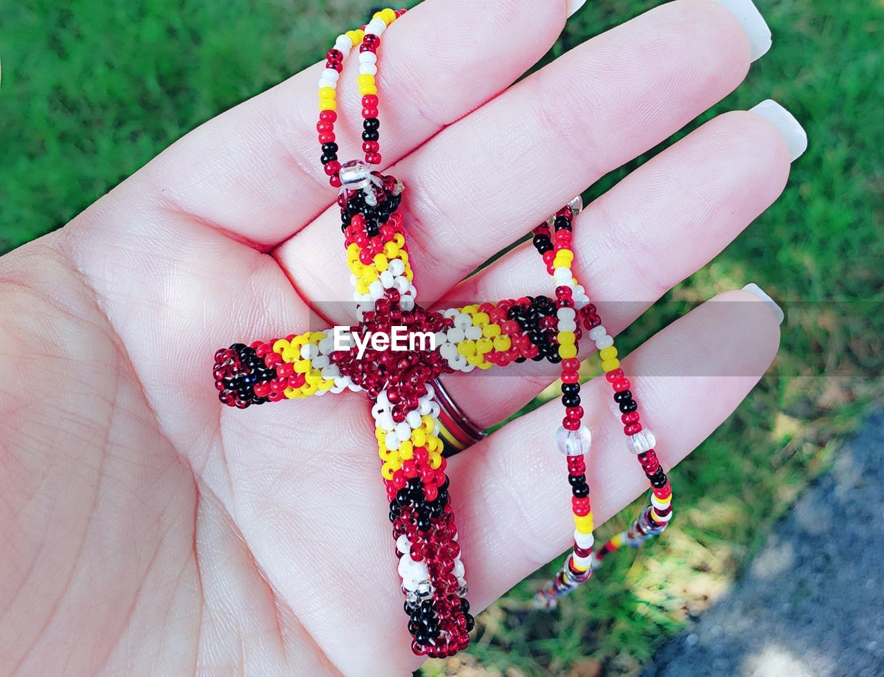 Cropped hand holding religious cross of beads outdoors