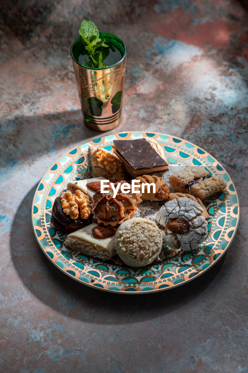 From above of baklava and biscuits with moroccan peppermint tea near knife and fork placed on table decorated with mint leaves