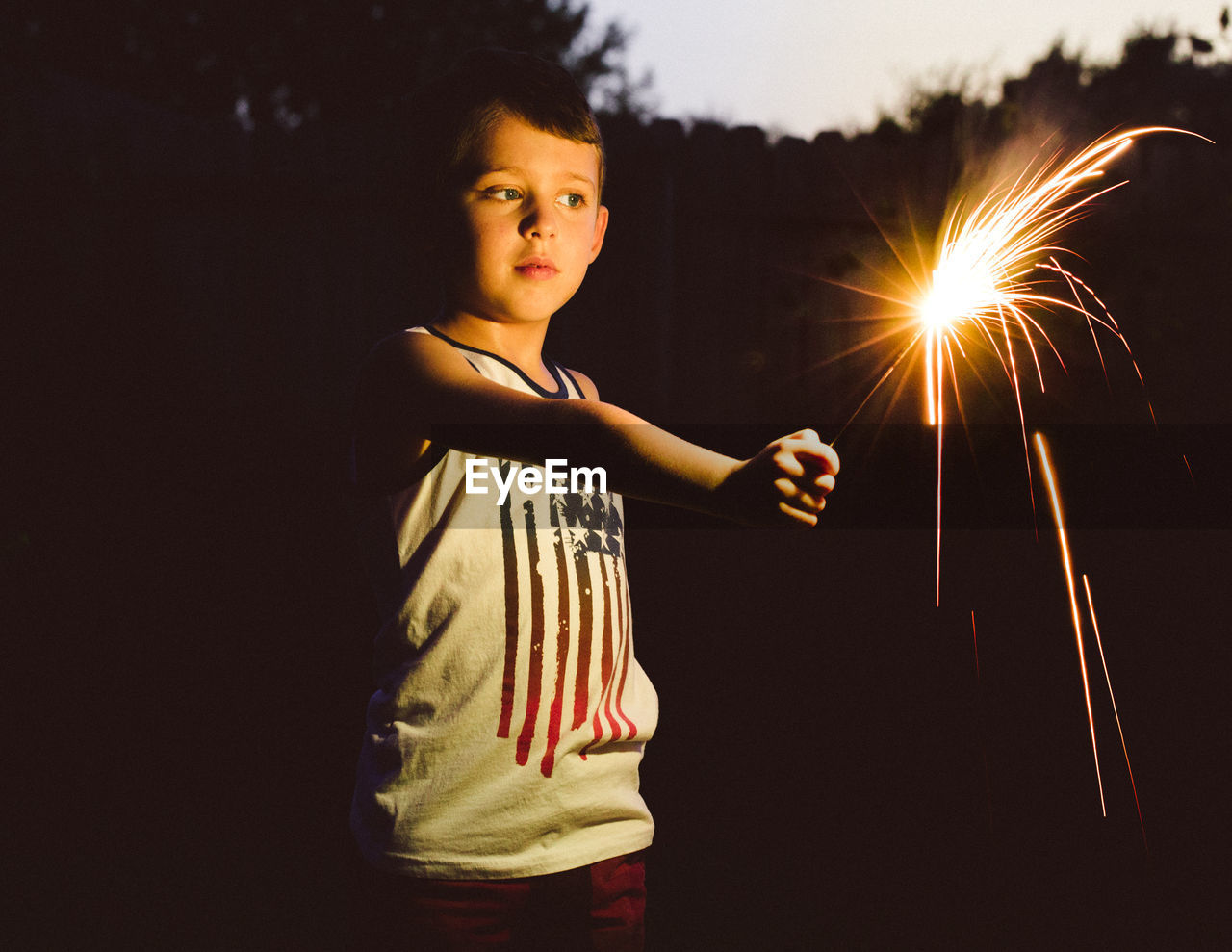 Cute boy holding sparkler standing outdoors