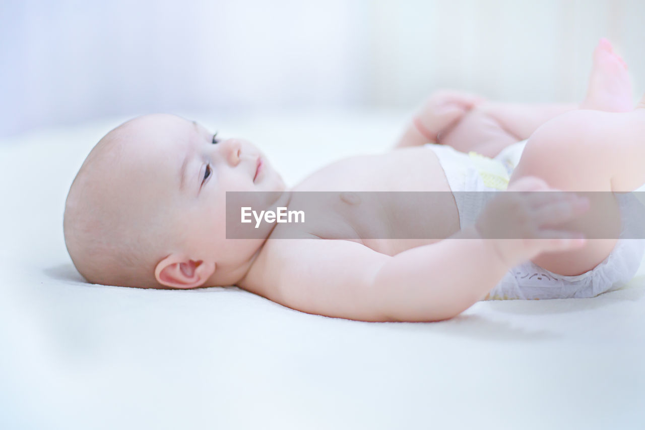 Cute shirtless baby boy lying on bed