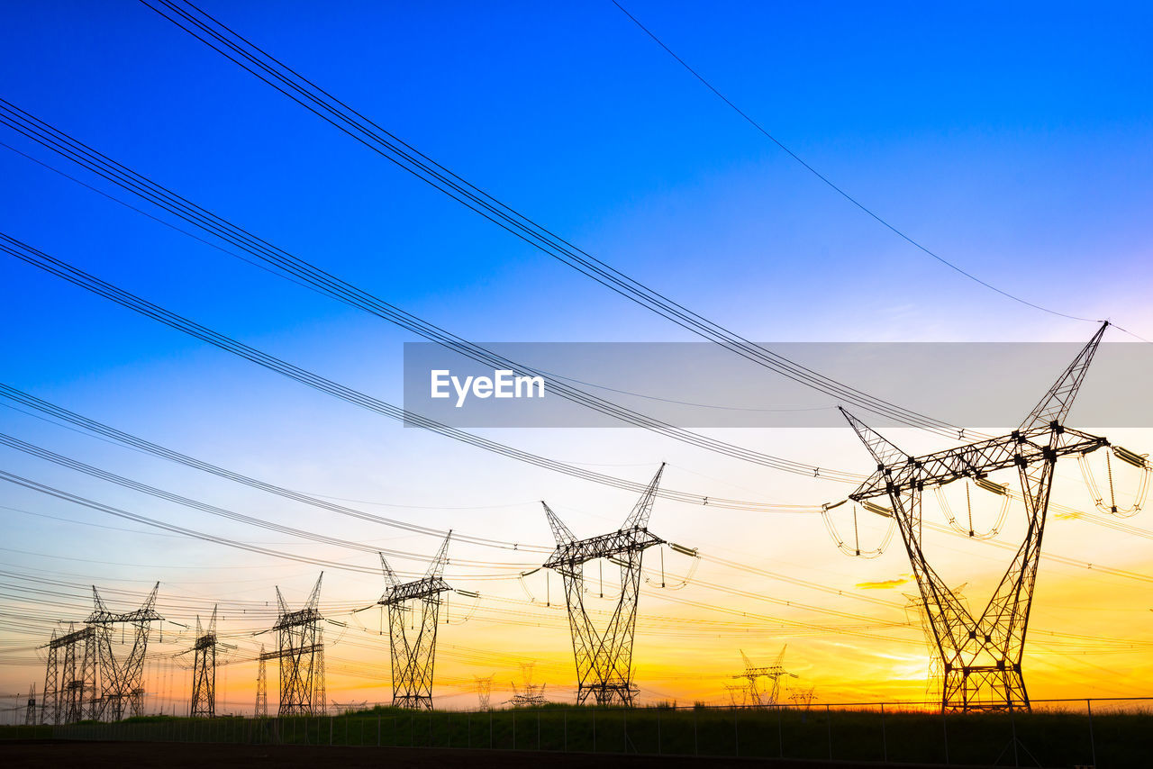 LOW ANGLE VIEW OF SILHOUETTE ELECTRICITY PYLONS AGAINST BLUE SKY