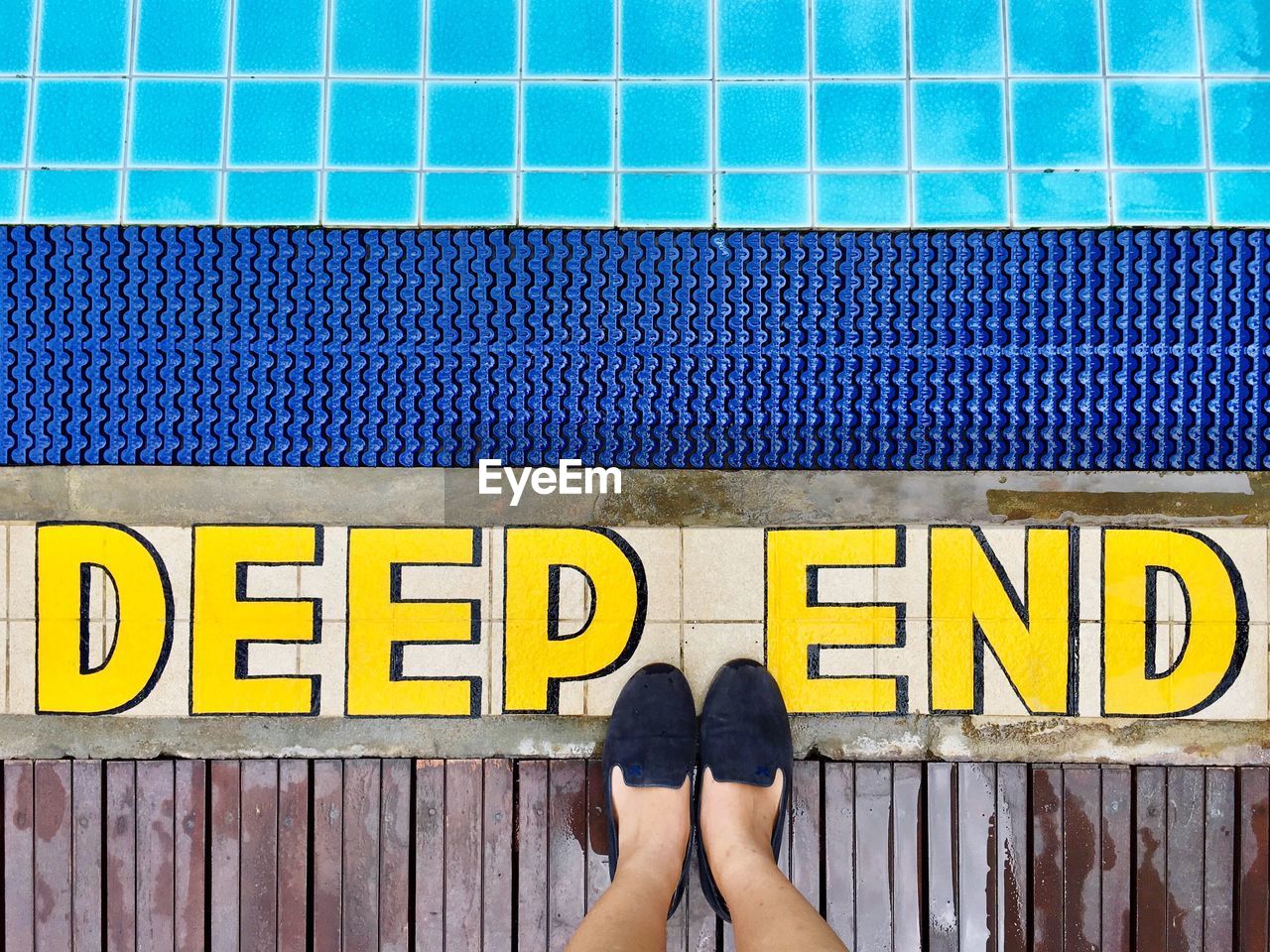 Low section of woman standing by yellow text on poolside