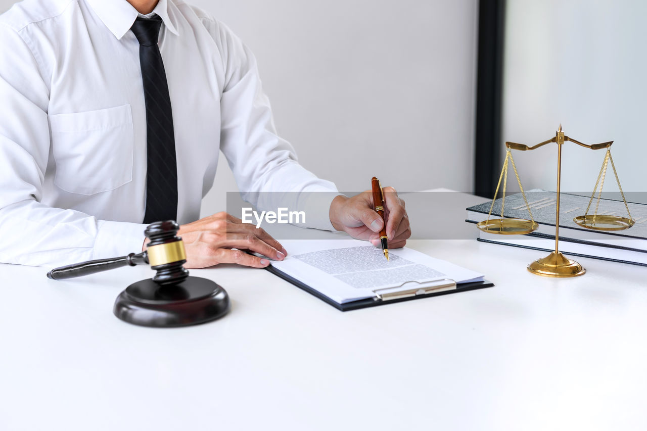Midsection of judge writing in book at table