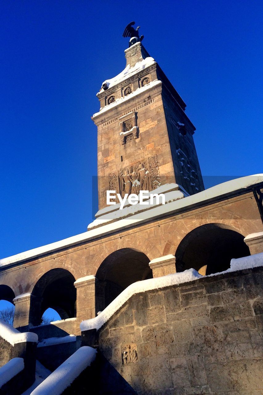 Low angle view of snow covered historic building against clear blue sky