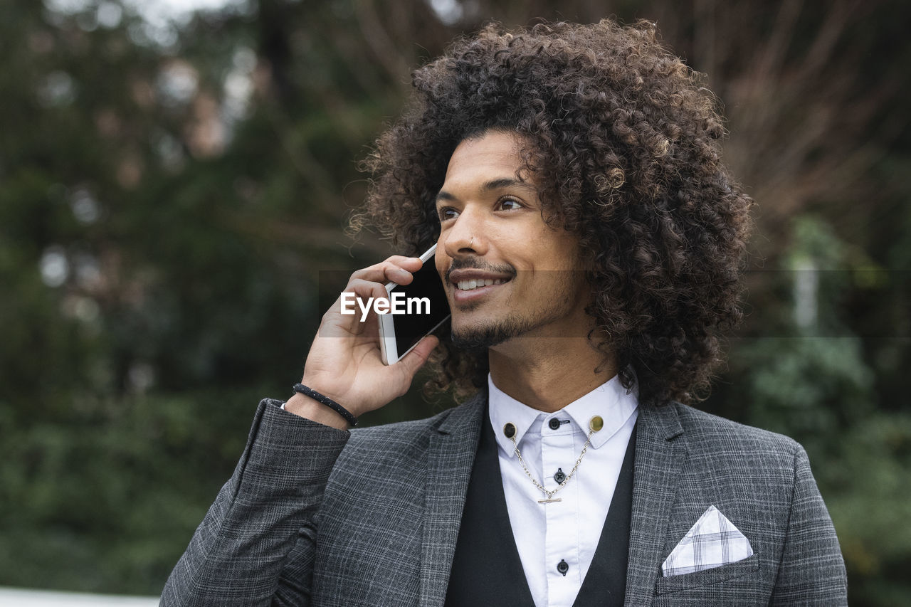 Smiling young businessman in nose ring talking through mobile phone