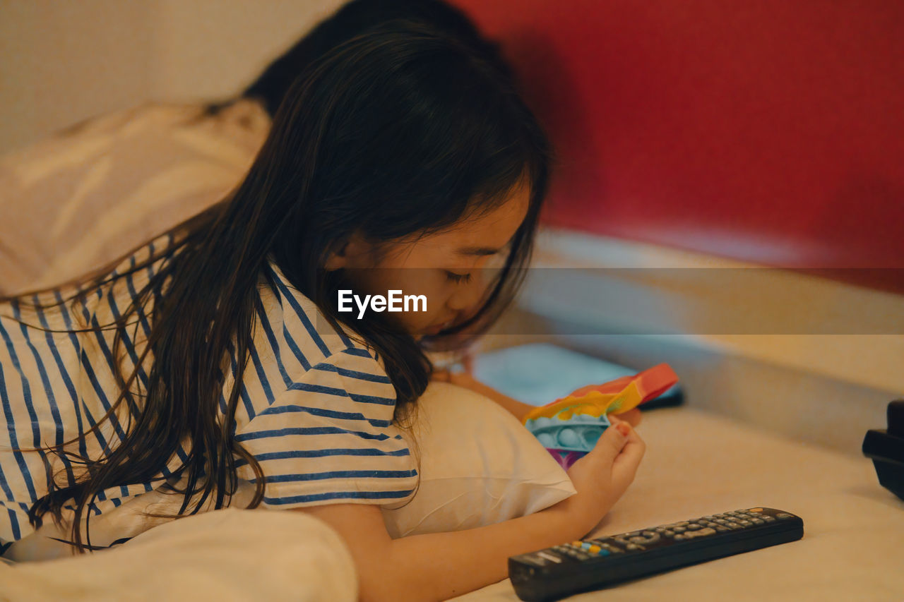side view of girl playing with toy on bed at home