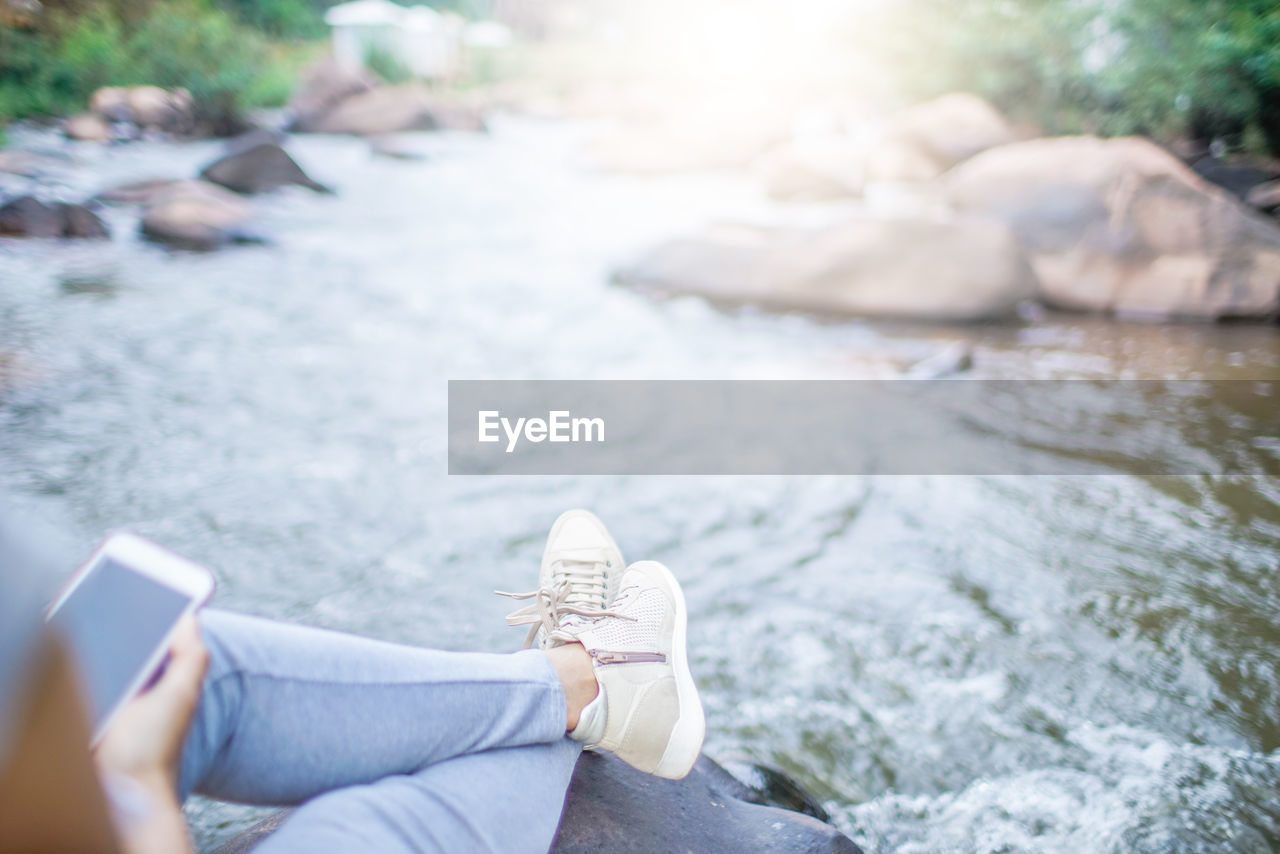 Low section of woman using mobile phone while sitting by river